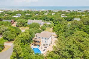 A residential area with houses surrounded by dense greenery, a swimming pool, and a view of the ocean.