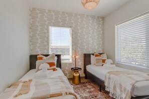 A bedroom with two beds, a patterned wall, a window, and a floor lamp.