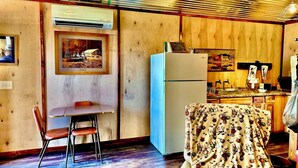 Une pièce chaleureuse avec des murs en bois, une table à manger avec des chaises, un réfrigérateur et un coin cuisine équipé d’un évier et d’un plan de travail.