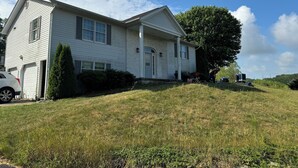 A two-story house with a front porch, a garage, and a large tree in the front yard. - Charming 3-bed countryside house in Northampton with WiFi and AC (Northampton)