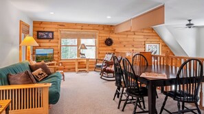 Un interior acogedor de cabaña con una mesa de comedor de madera, sillas, un sofá y un televisor.