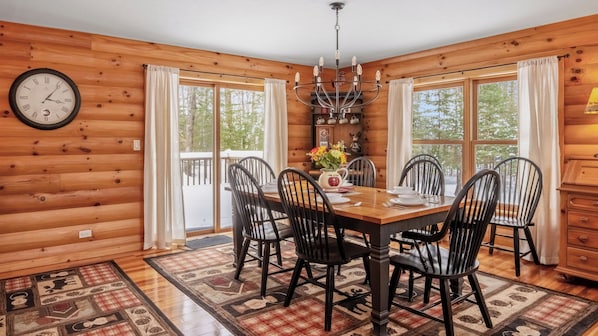 A wooden cabin dining room with a table set for four, chairs, a chandelier, and a clock on the wall.