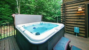 A hot tub on a wooden deck with a wooden cabin in the background.