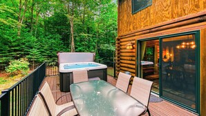 Una cabaña de madera con jacuzzi, mobiliario exterior y un ventanal de vidrio que da a un interior acogedor.