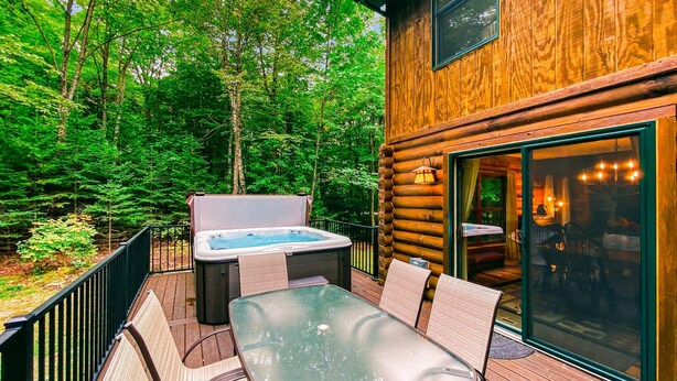 Una cabaña de madera con jacuzzi, mobiliario exterior y una puerta de vidrio que da a un comedor interior.
