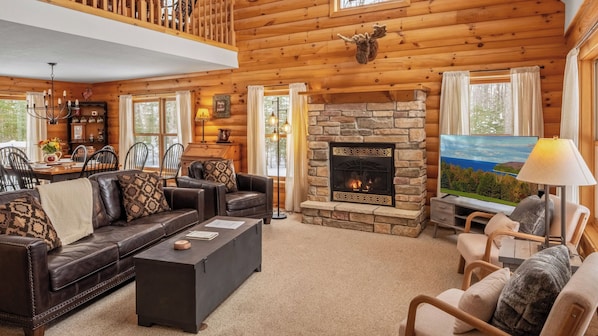 A cozy log cabin interior with a stone fireplace, leather furniture, and a television.