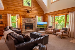 A log cabin interior with a fireplace, leather sofa, and a television.
