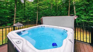 Un jacuzzi en una terraza rodeada de barandilla de madera, con una hamaca y árboles frondosos al fondo.