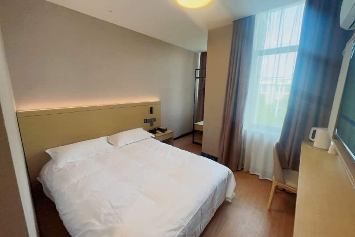 Une chambre d’hôtel avec un lit, une table de chevet, une lampe et une fenêtre avec des rideaux.