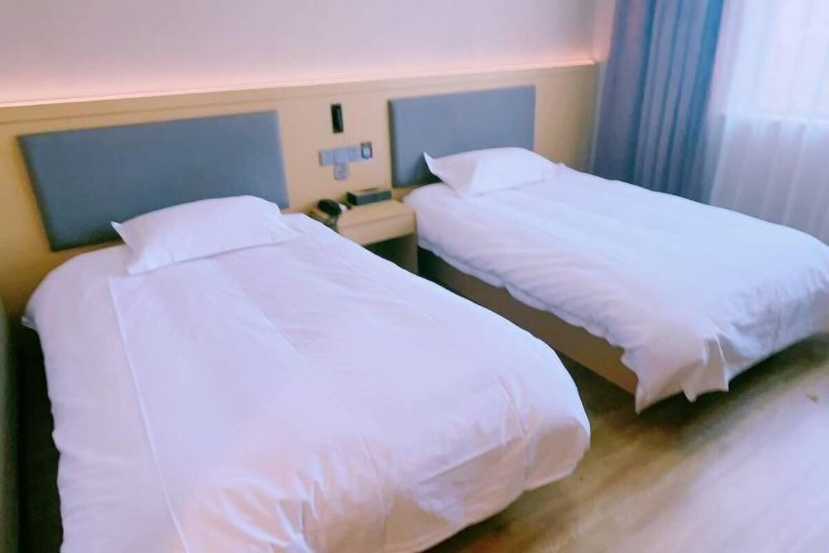 Deux lits simples avec du linge de lit blanc, une table de chevet avec un téléphone et une tête de lit dotée d’un interrupteur pour la lumière.