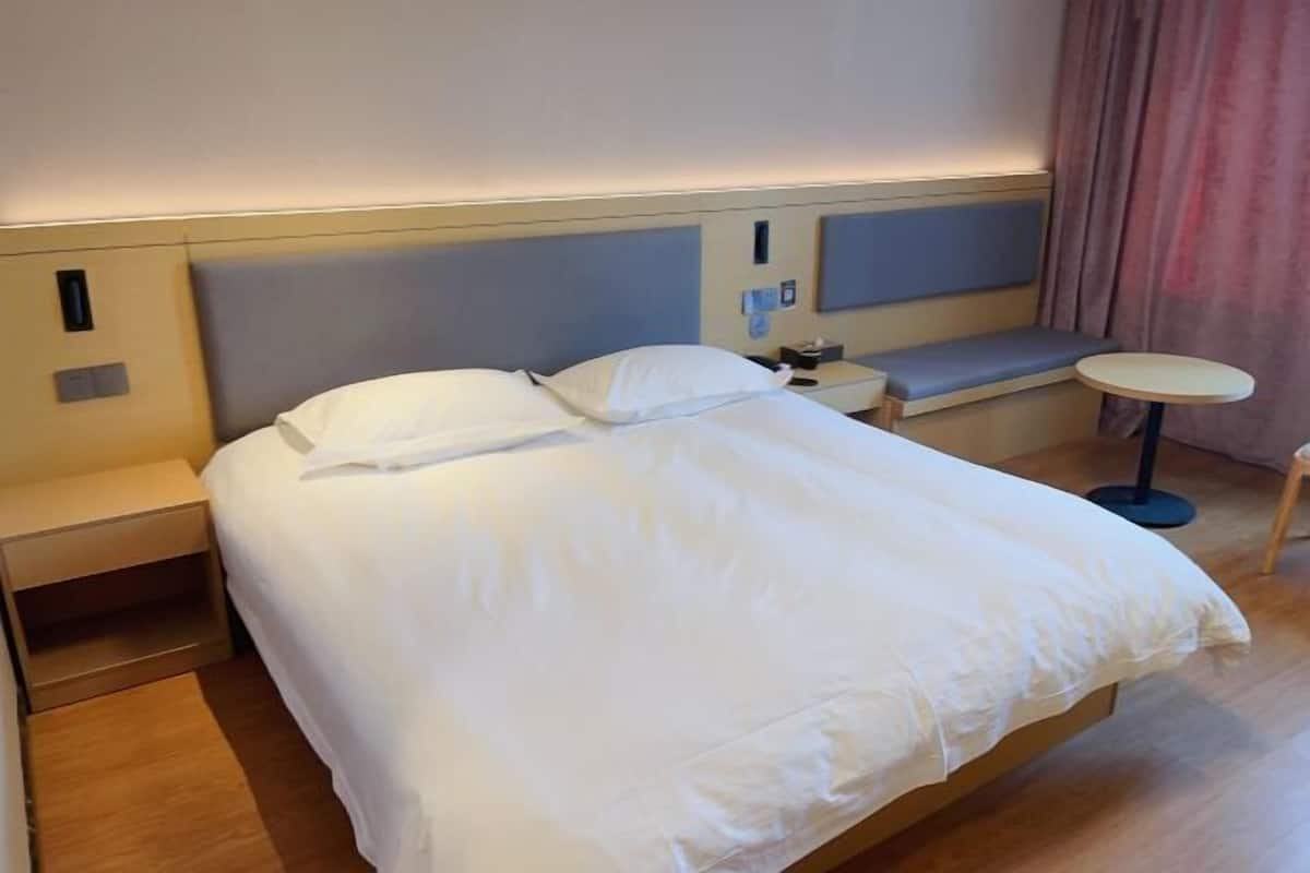 Un lit bien fait, avec du linge de lit blanc, une table de chevet avec une lampe et une petite table ronde.