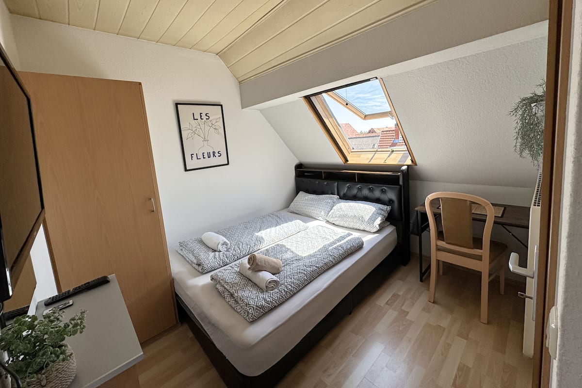 A small, compact bedroom with a loft-style bed, a desk, and a skylight.