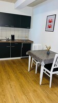 Uma cozinha com armários pretos, bancada branca e uma mesa de jantar com cadeiras brancas.