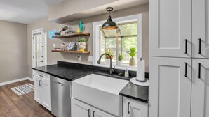 Una cocina con armarios blancos, encimera negra, lavavajillas de acero inoxidable y ventana con vistas al exterior.
