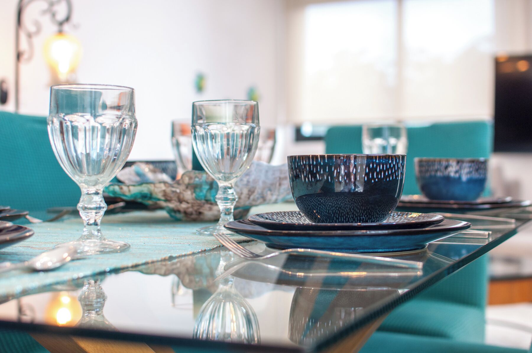 Et spisebord med klare glas og en blå skål, placeret på en teal dug.