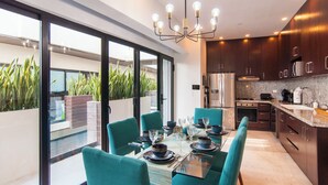 Een moderne keuken met donkerhouten kastjes, roestvrijstalen apparatuur en een eethoek met teal stoelen en een glazen tafel.