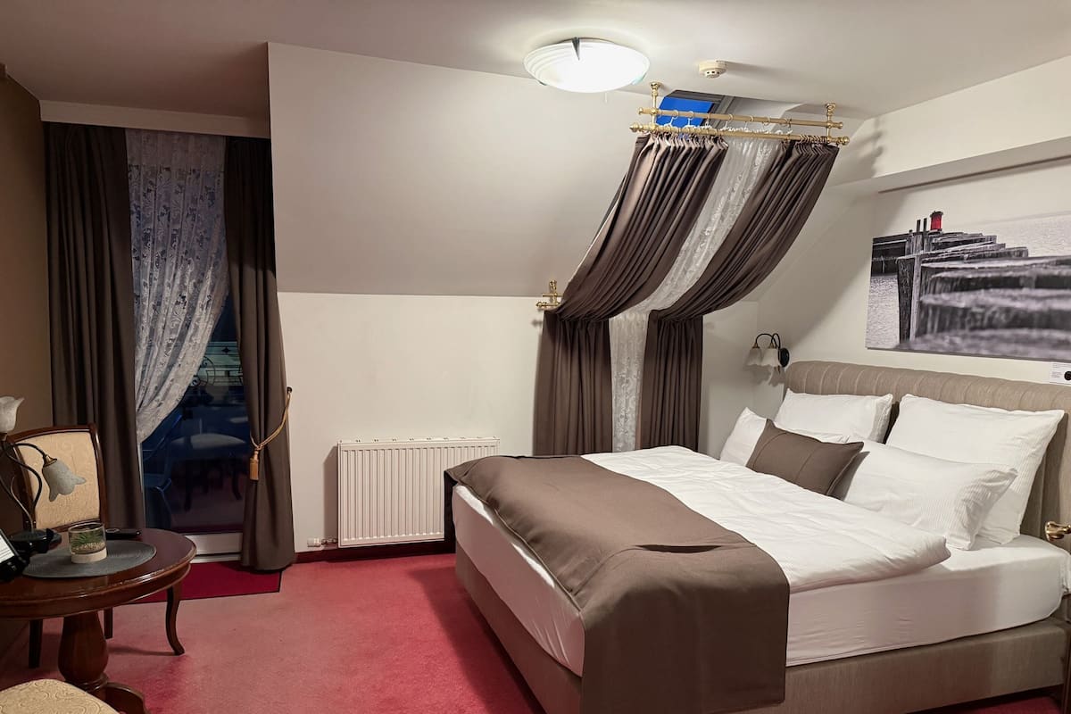 A hotel room with a bed, a radiator, a table with chairs, and curtains.