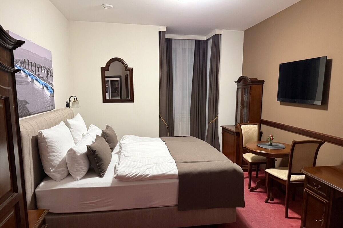 A hotel room with a bed, a desk, a chair, a television, and a window with curtains.