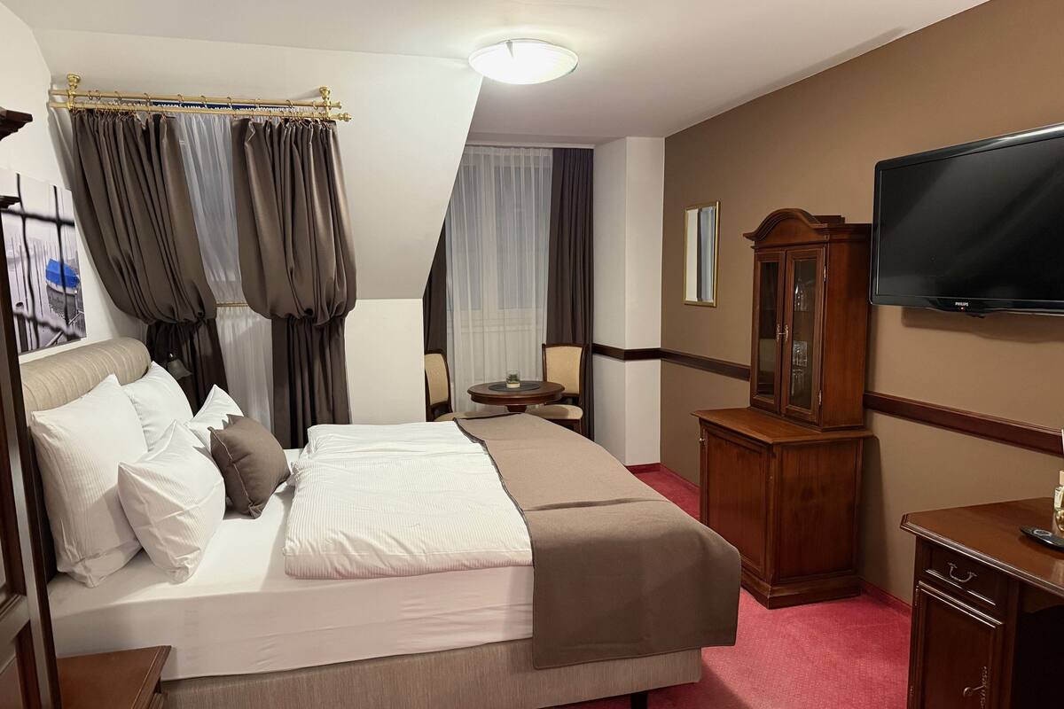 A hotel room with a large bed, a wooden cabinet, a television, and a small table with a chair.