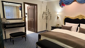 Hotellihuone, jossa on suuri sänky, lipasto, penkki, peili, kattokruunu ja ovi.