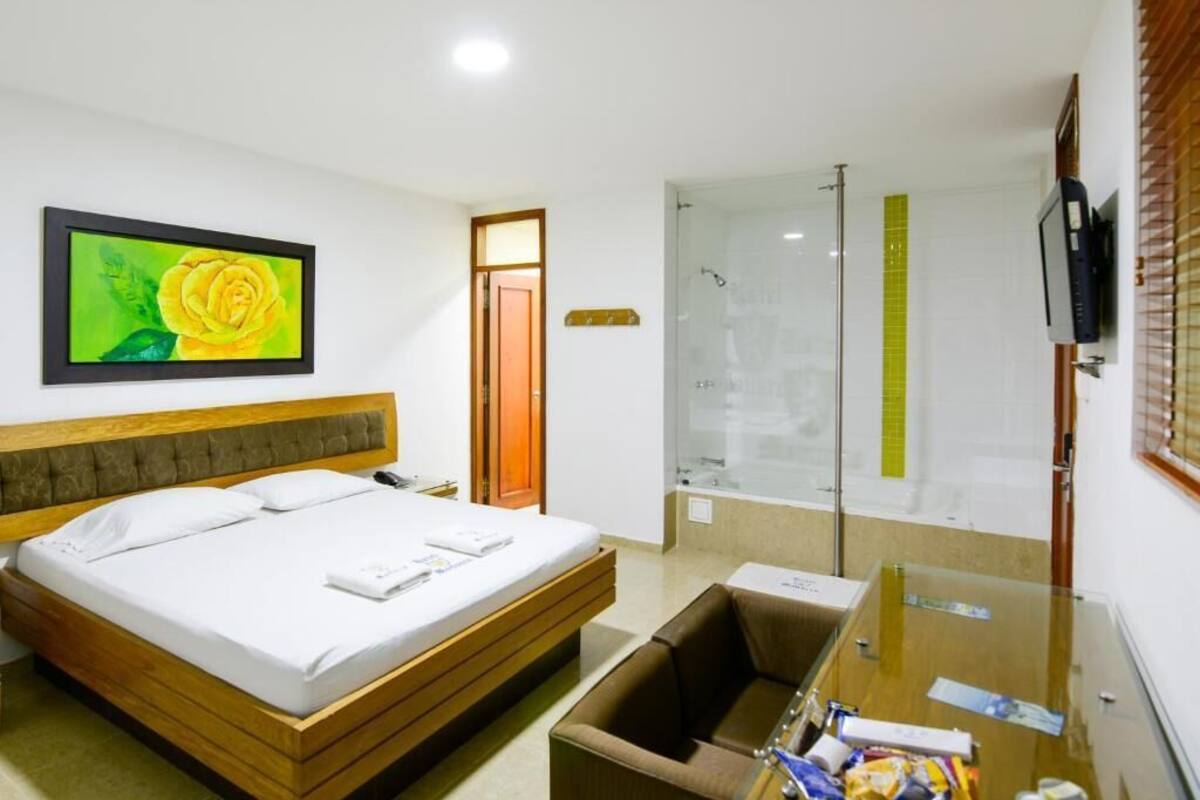 A hotel room with a bed, a desk, a chair, a shower, and a TV.