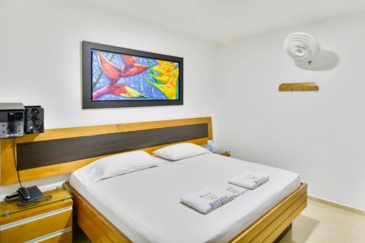 A neatly made bed with white linens and a colorful abstract painting above it.