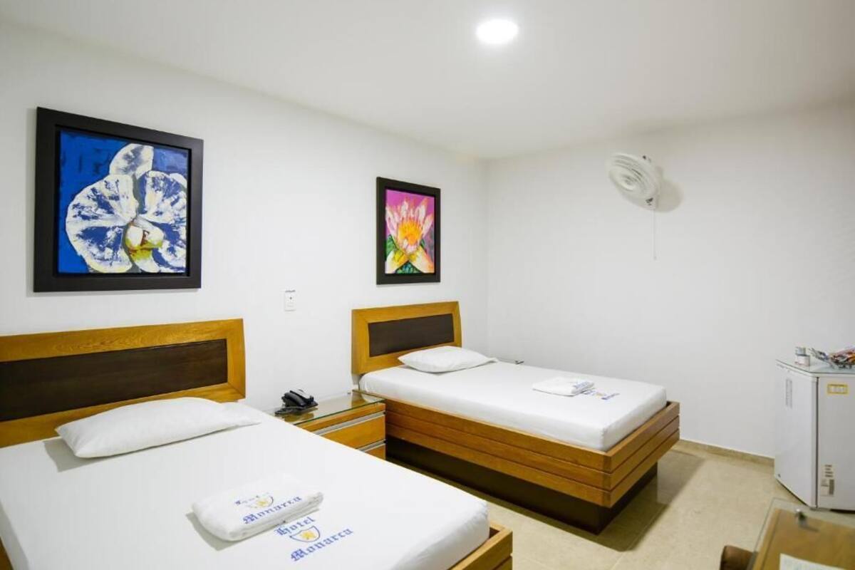 A hotel room with two single beds, a small desk, a cabinet, and two framed artworks on the wall.