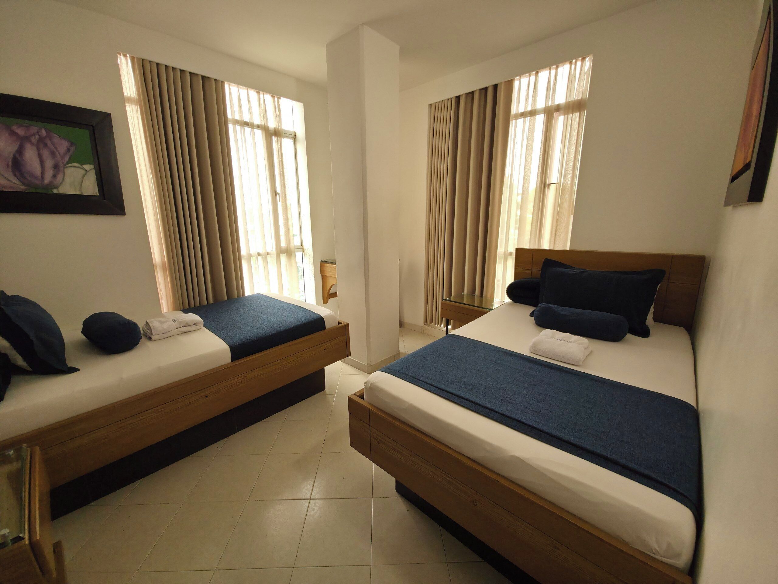 Een hotelkamer met twee eenpersoonsbedden, een klein nachtkastje, een spiegel en een raam met gordijnen.