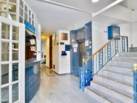 Zona de recepción de un hotel con mostrador, una escalera con barandillas azules y un cartel que indica la recepción.