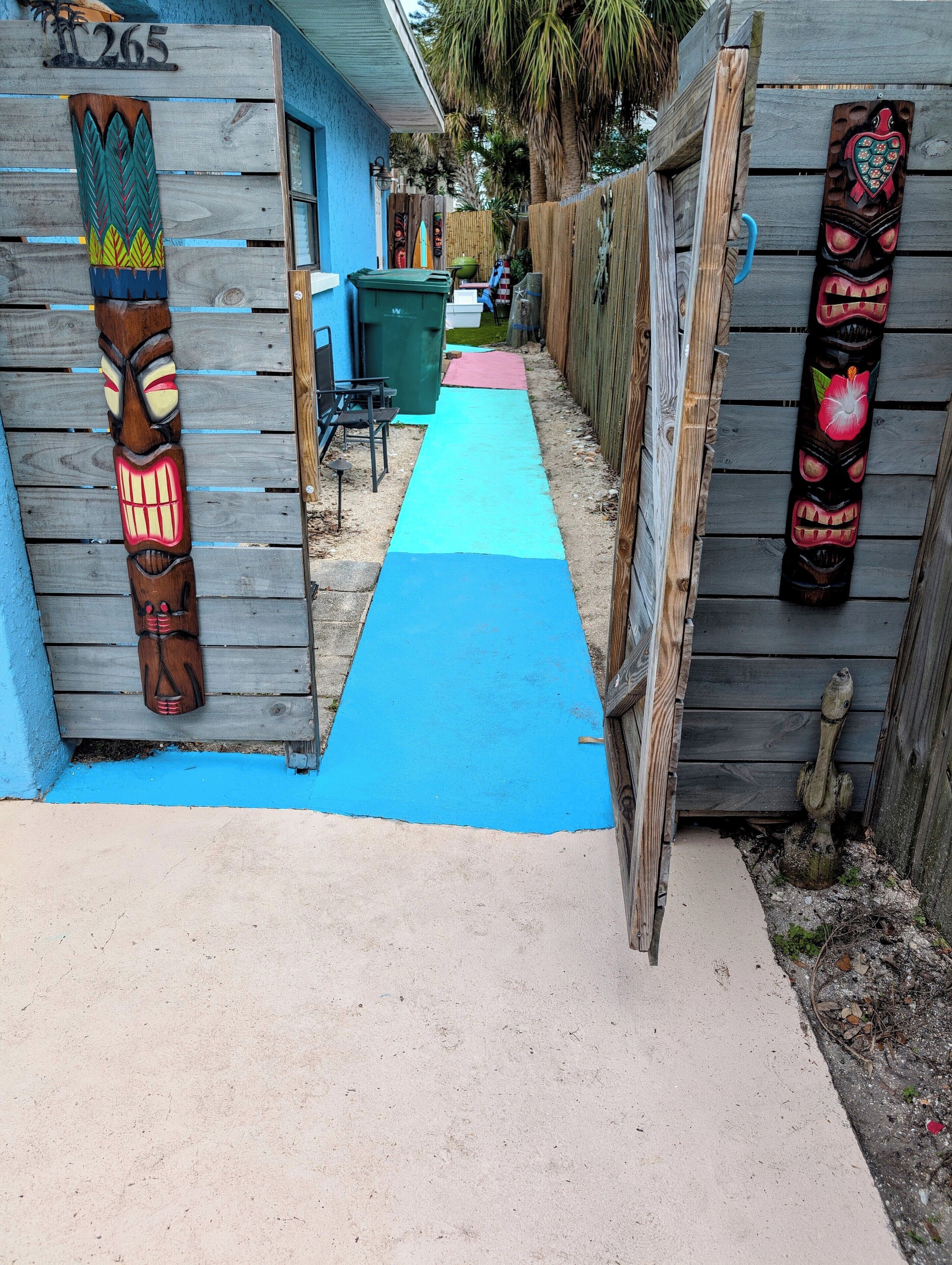 A narrow pathway leading to a wooden structure with totem poles and a number '265' sign.