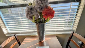 A dining table with a metal vase containing flowers, a menu, and two wooden chairs. - King Studio Steps from Sand + Resort Backyard (Cocoa Beach)