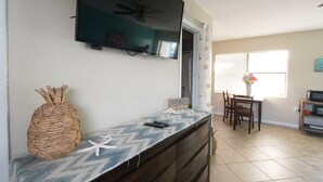A kitchen with a TV mounted above a counter, a woven pineapple decoration, and a sign that says "BEACH life is best". - King Studio Steps from Sand + Resort Backyard (Cocoa Beach)