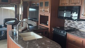A compact kitchen with wooden cabinets, a black stove, a microwave, and a sink. - Cozy RV with Expansive River Views (Newcastle)