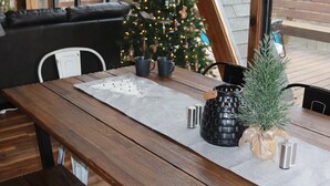 Een gezellig eetgedeelte met een houten tafel, bankjes, een kerstboom en uitzicht door grote ramen.