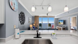 A modern kitchen with a large window, a sink, and a dining area with a view of the ocean. - Tidewater Escape: 1br/2ba Beachfront Condo, Sleeps 6, Gulf Views & Comfort! (Panama City Beach)