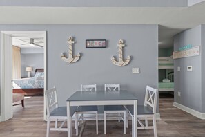 Un coin repas avec une table et des chaises, un ventilateur de plafond et une vue sur une chambre à coucher avec un lit et une table de chevet.