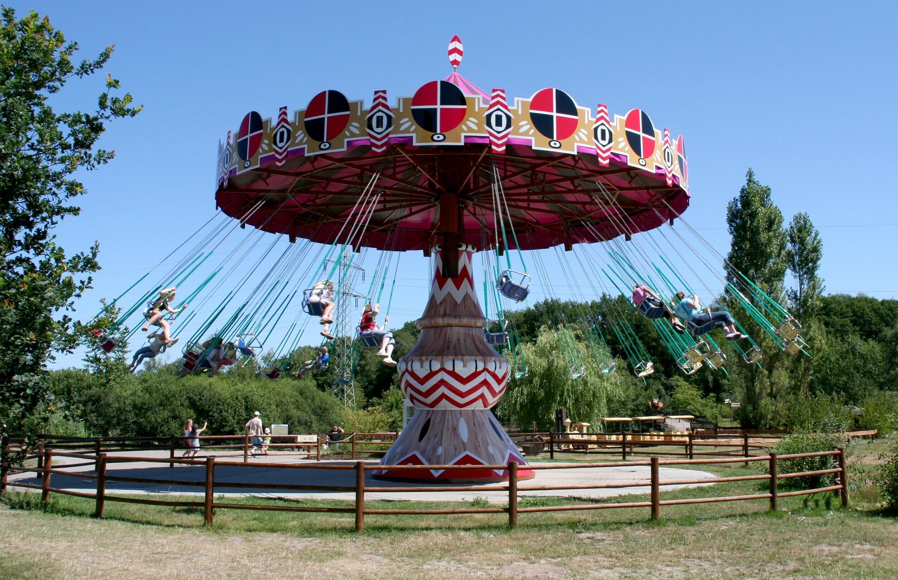 A carousel with multiple seats and a central pole, surrounded by a fenced area with benches.