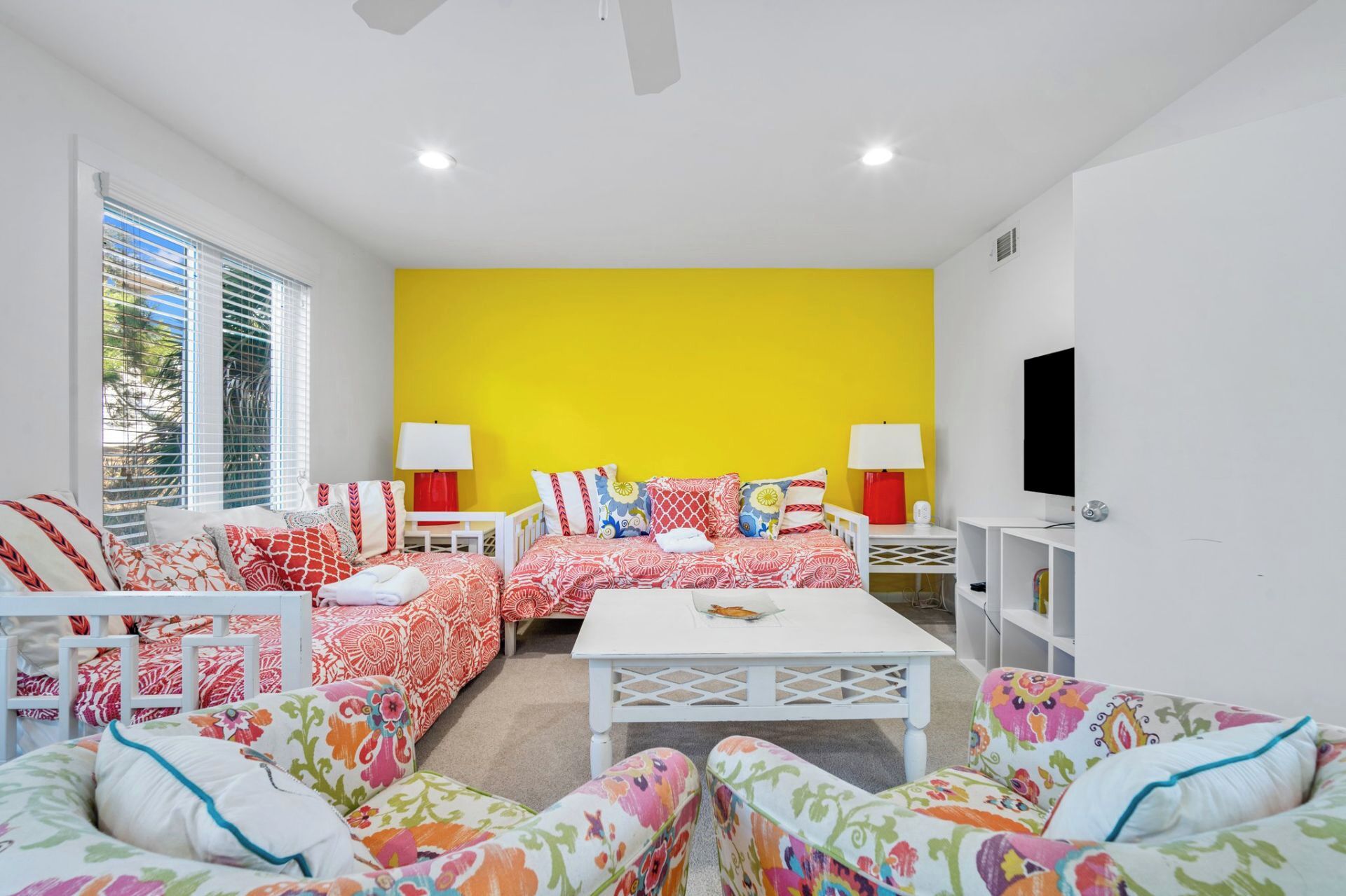 A bright living room with a yellow accent wall, white furniture, and a TV mounted on the wall.