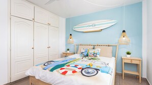 Un dormitorio con una cama, una decoración de tabla de surf, dos mesitas de noche con lámparas y un armario.