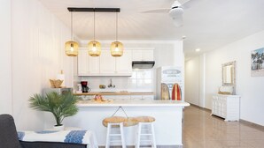 Una cocina moderna con armarios blancos, una isla central con taburetes, luces colgantes y un ventilador de techo.