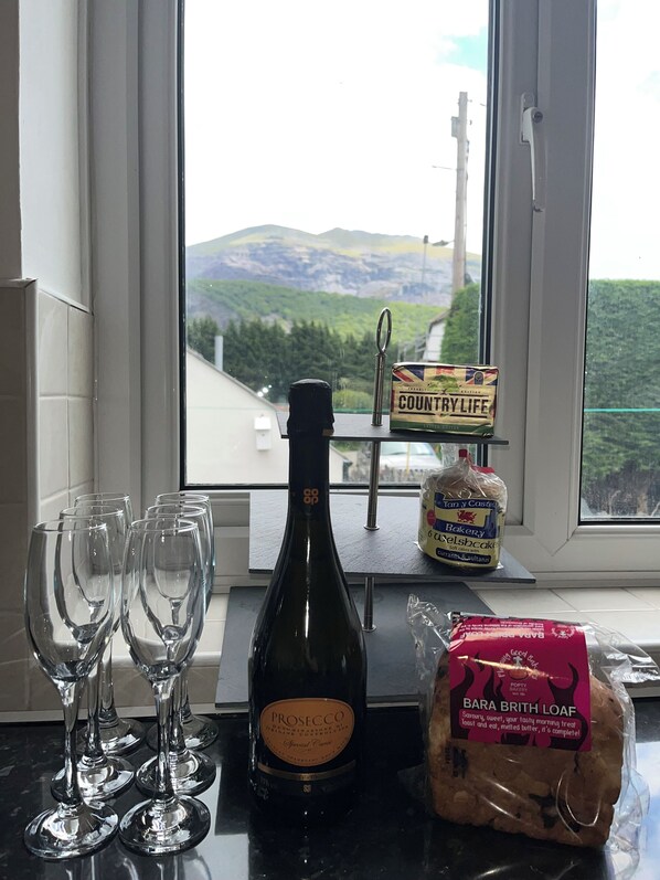 A kitchen counter with wine glasses, a bottle of Prosecco, a loaf of Bara Brith Loaf, and a bag of bread.