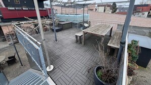 A rooftop terrace with a wooden table and benches, a metal railing, and a potted plant. - Tiny House "Black Pearl" (Tettnang)