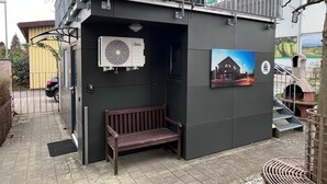 A small outdoor seating area with a bench, a wall-mounted air conditioning unit, and a framed picture of a building. - Tiny House "Black Pearl" (Tettnang)
