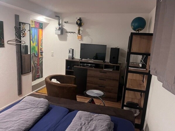 Une petite pièce comprenant un lit, un bureau avec un ordinateur, une chaise et un téléviseur.