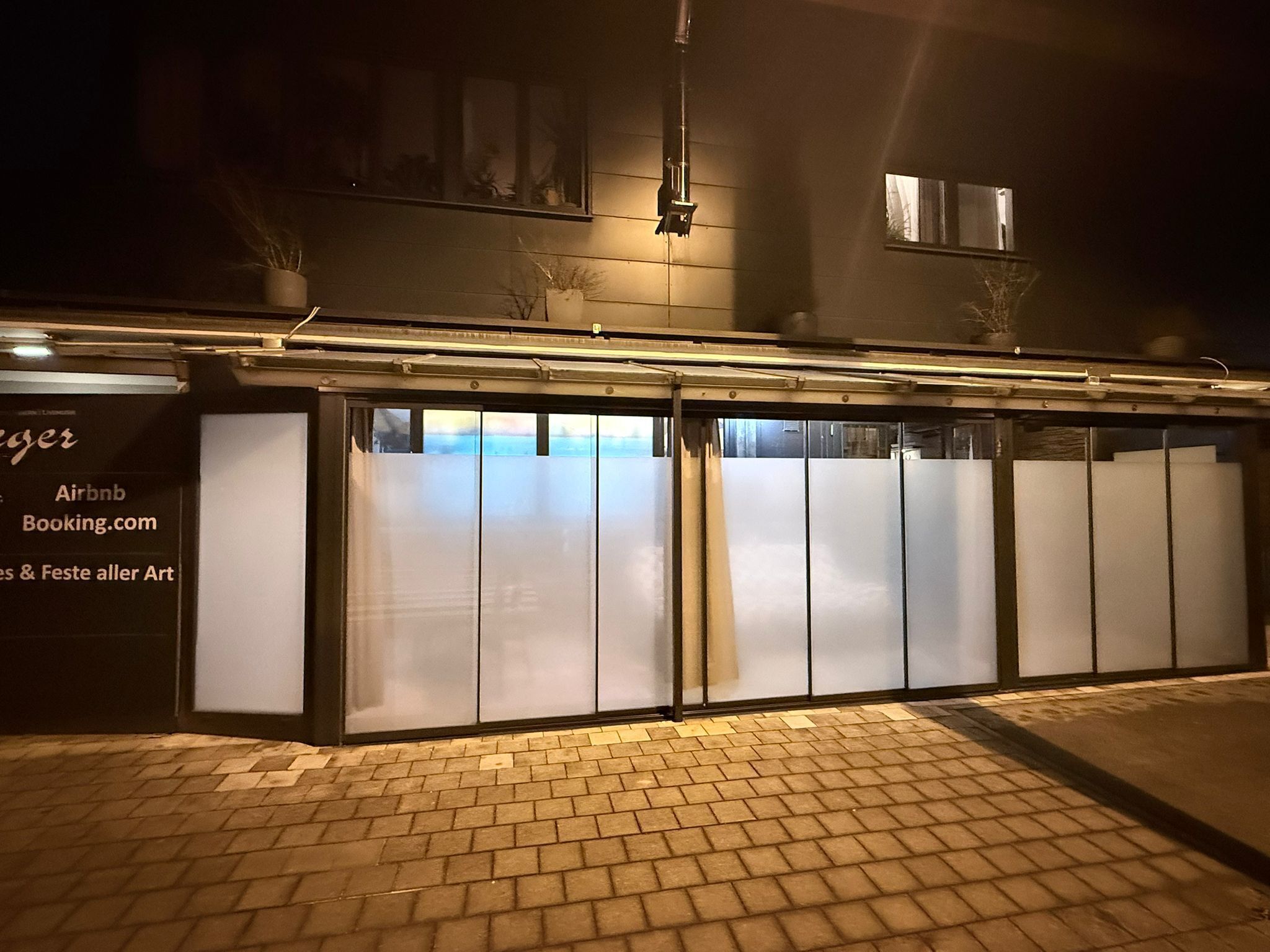 Ein Gebäude mit Glasfassade, einem Schild mit Airbnb und Booking.com sowie einem Pflasterhof.