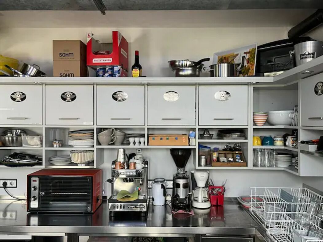 Une cuisine avec des meubles blancs, un grille-pain rouge, une machine à café et divers ustensiles de cuisine.