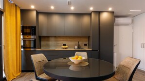 Una cocina moderna con una mesa redonda de cristal, dos sillas y un cuenco de fruta.