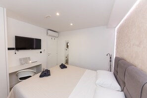 A hotel room with a bed, a desk with a flat-screen TV, a hairdryer, and a shower area.