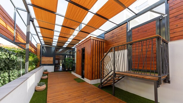 Una terraza moderna al aire libre con piso de madera, techo de cristal y escalera de metal.