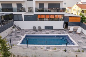 A modern residential building with a rooftop swimming pool, outdoor seating, and a staircase leading to a balcony.